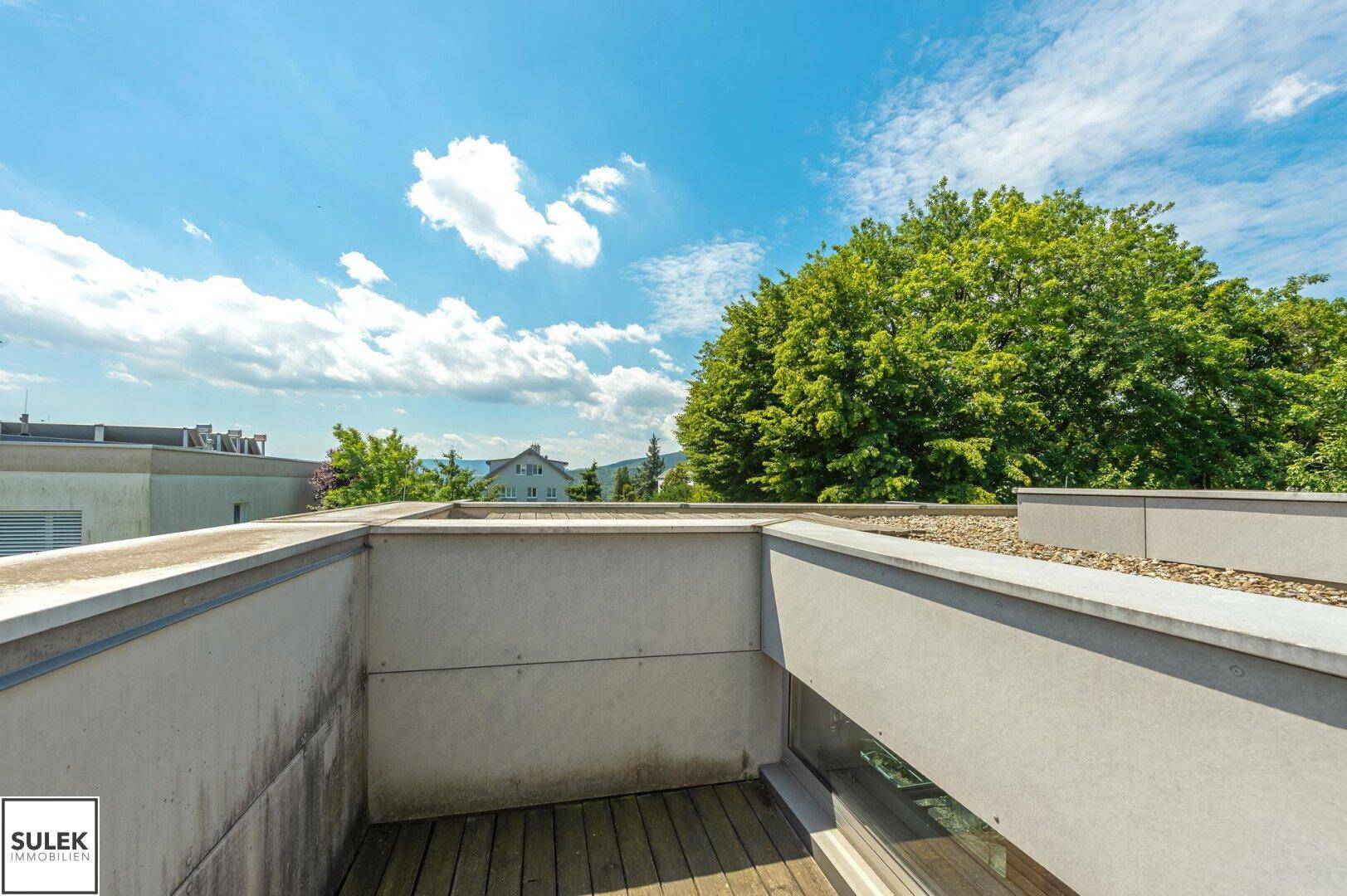 Geräumige Dachterrasse mit Holzdielen und weitem Blick auf die Umgebung und den blauen Himmel.