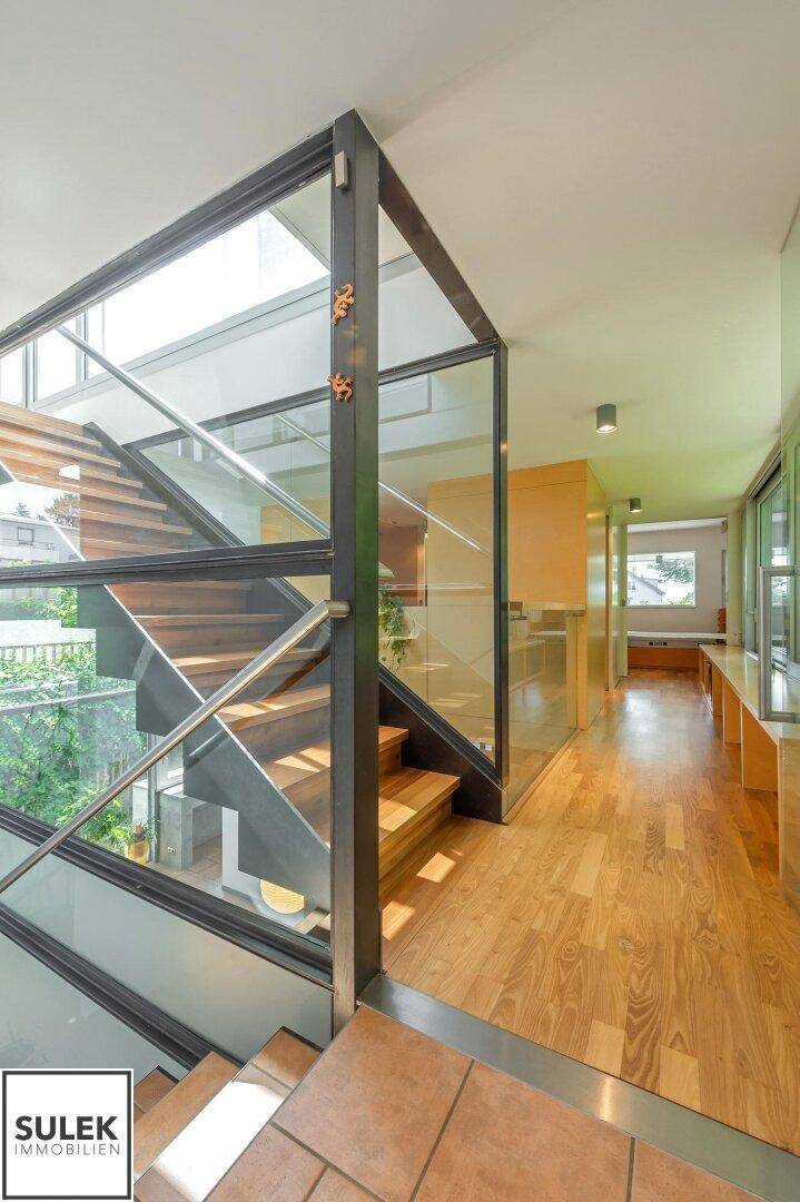Elegante Treppe mit Glasgeländer und Holzstufen, die das moderne Design des Hauses unterstreicht.