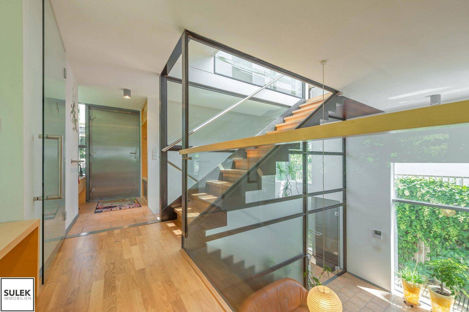 Offene Treppe mit Glasgeländer und Holzboden, die den Blick in den unteren Bereich freigibt.