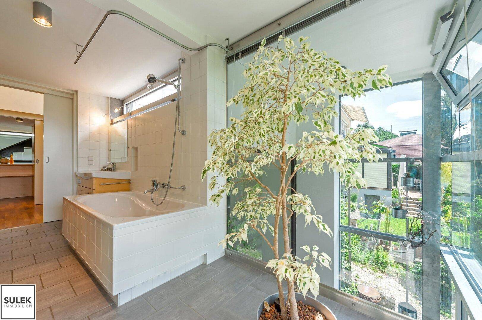 Helles Badezimmer mit Badewanne, Waschbecken und großen Fenstern mit Blick ins Grüne, sehr entspannend.
