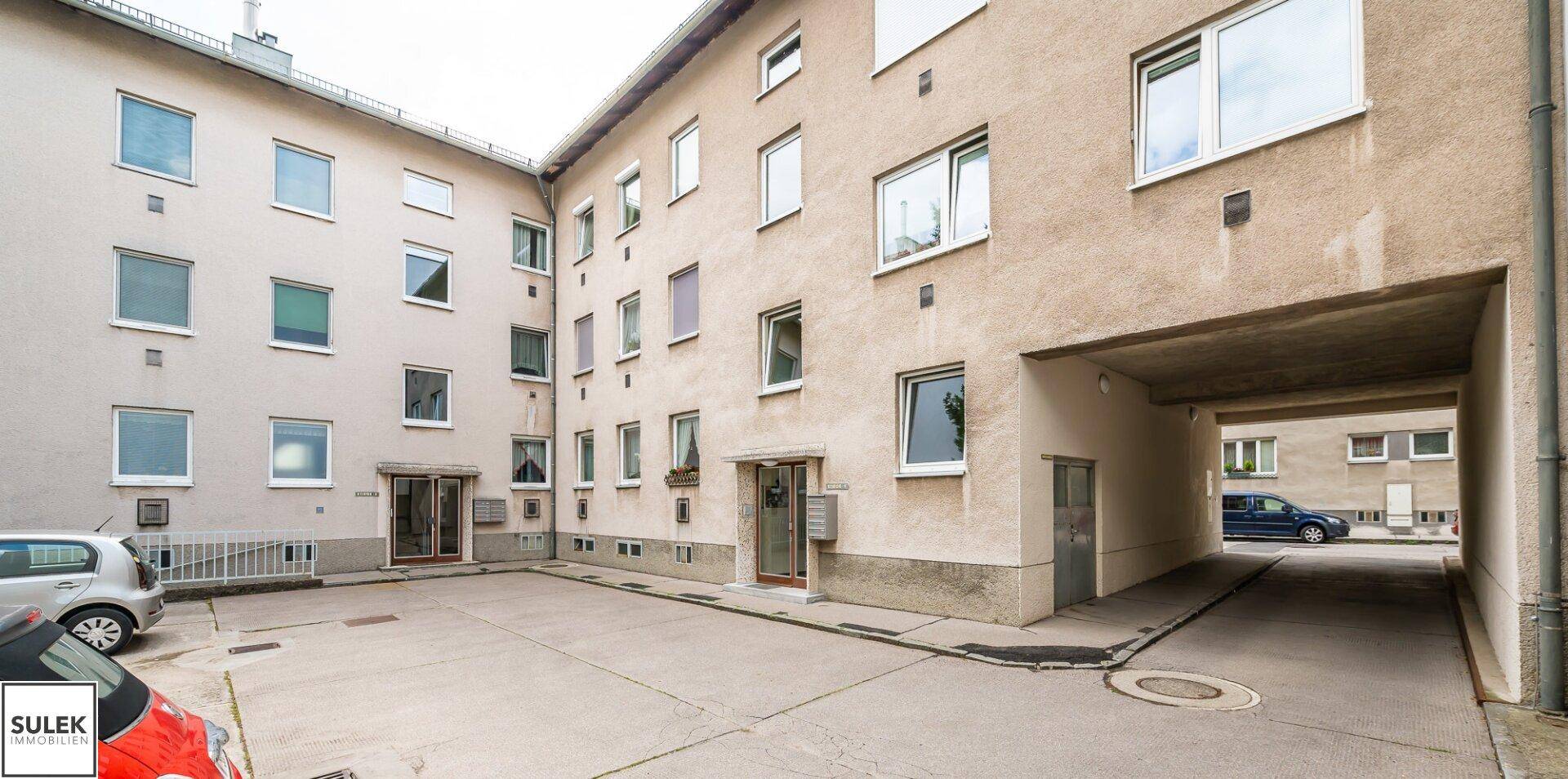 Innenhof eines Mehrfamilienhauses mit gepflastertem Bereich und Durchfahrt.