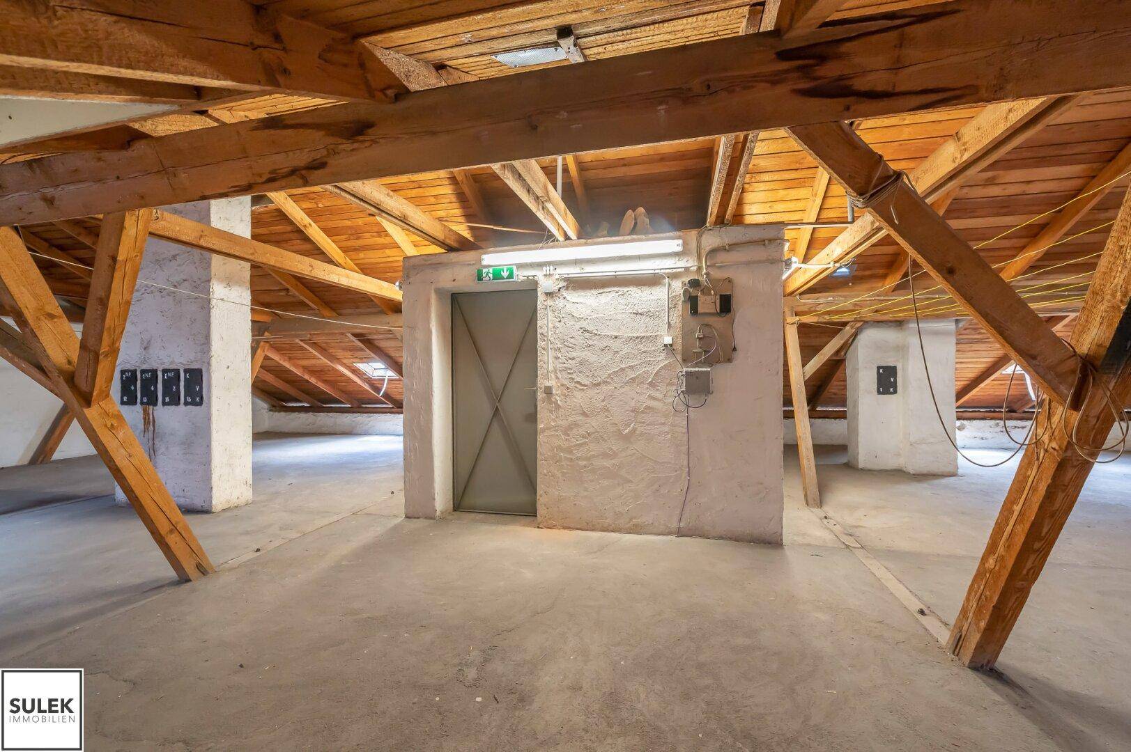 Dachbodenbereich mit sichtbaren Holzbalken und einem Aufzugzugang.