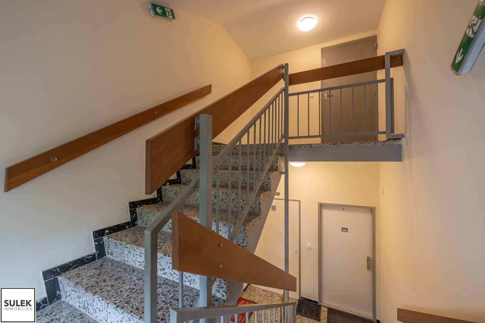 Treppenhaus mit Terrazzostufen und Metallgeländer in einem Mehrfamilienhaus.