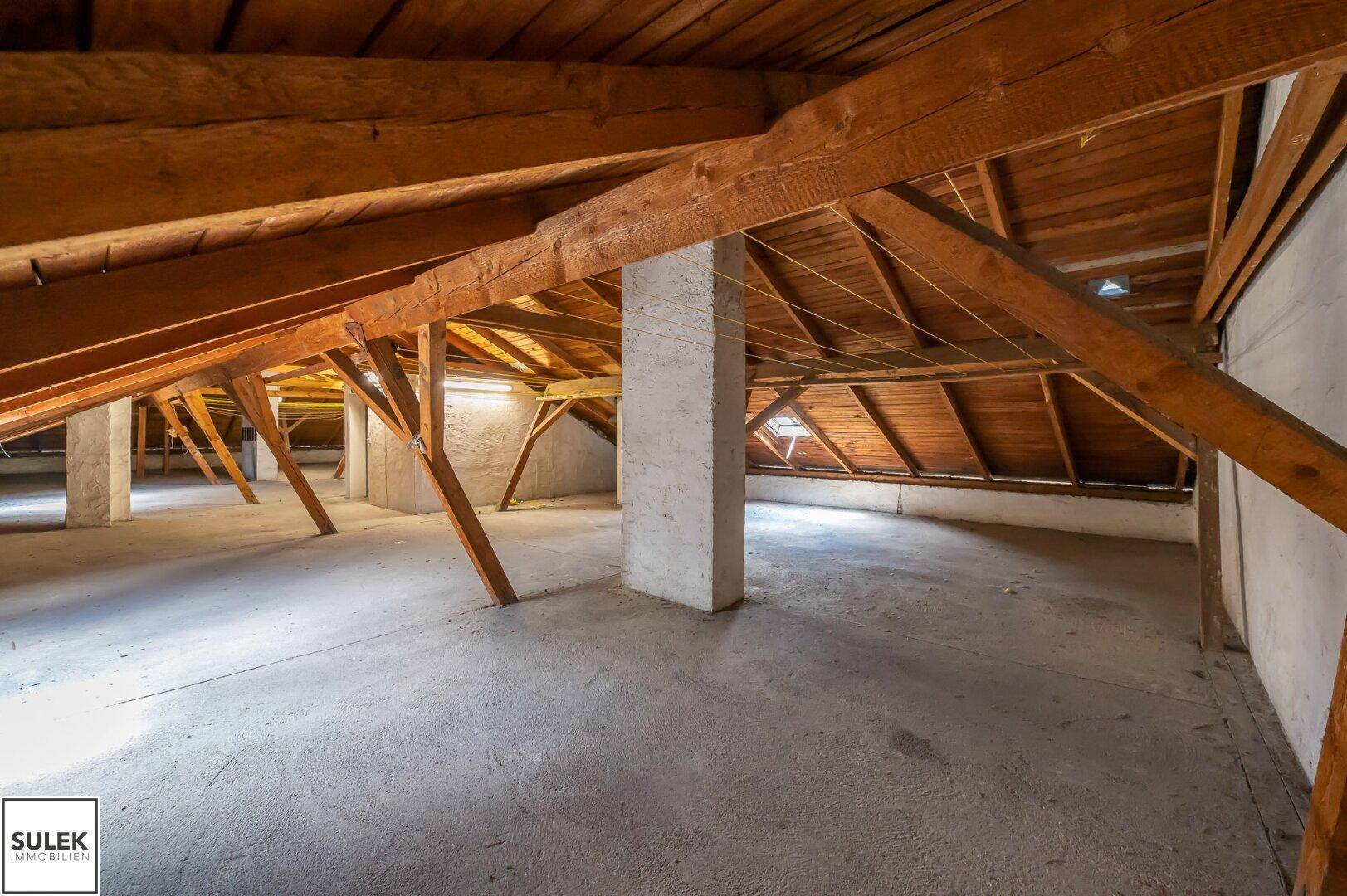 Geräumiger Dachboden mit freiliegenden Holzbalken und schrägen Decken, bietet viel Licht.