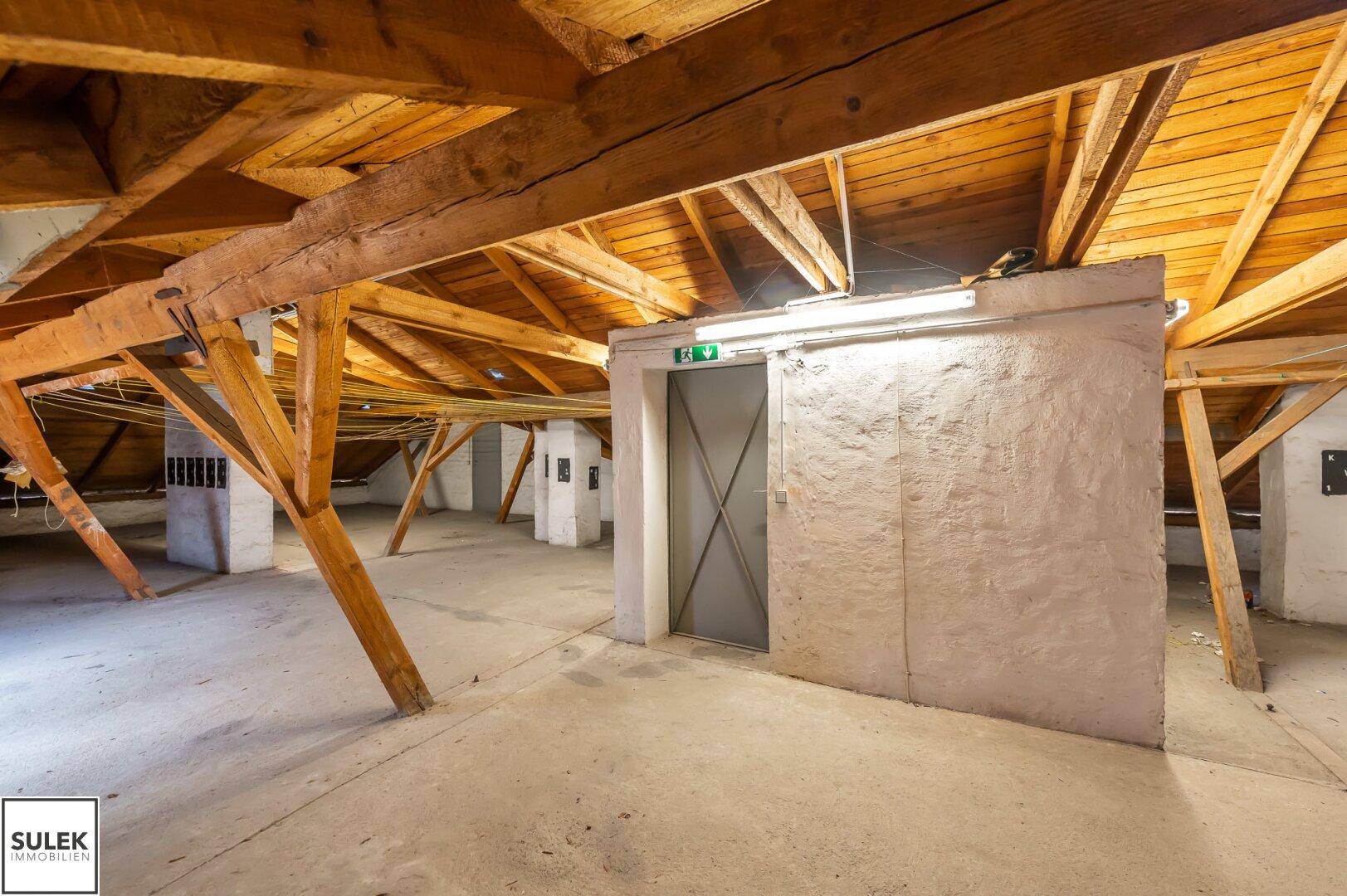 Dachbodenbereich mit sichtbaren Holzbalken und einem Aufzugzugang.