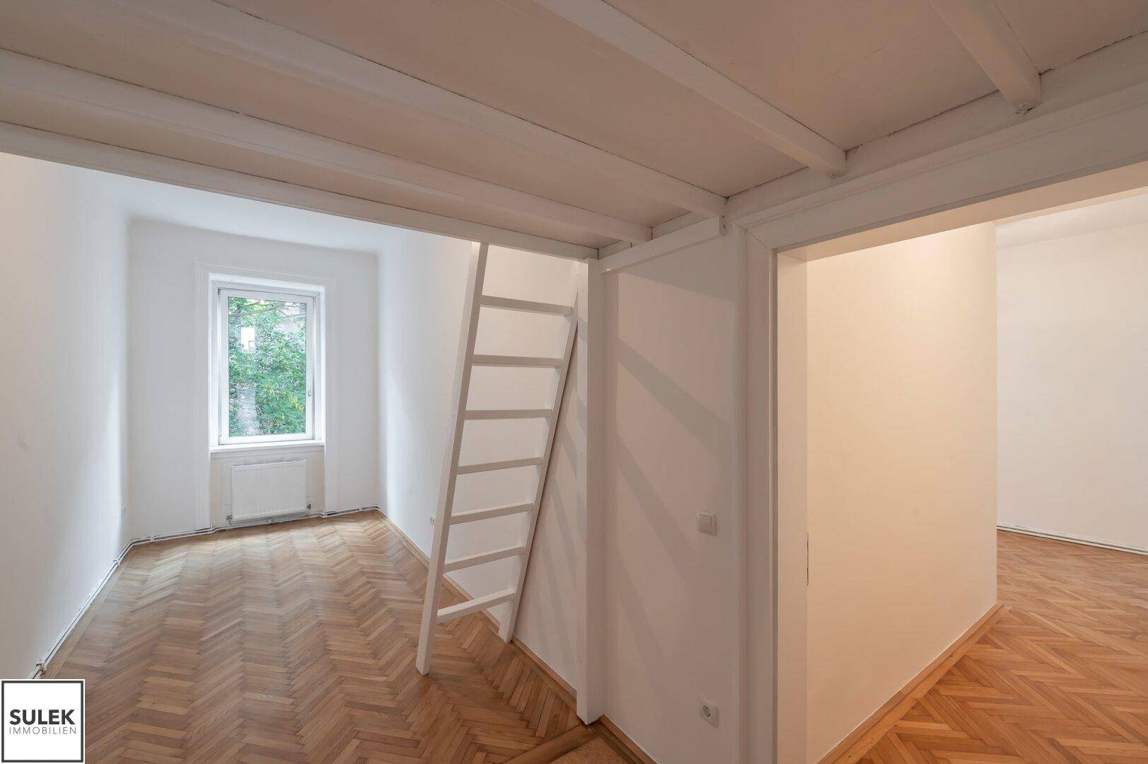 Kleineres Zimmer mit Hochbettkonstruktion, Fischgrätparkett und Fenster zum Grünen.