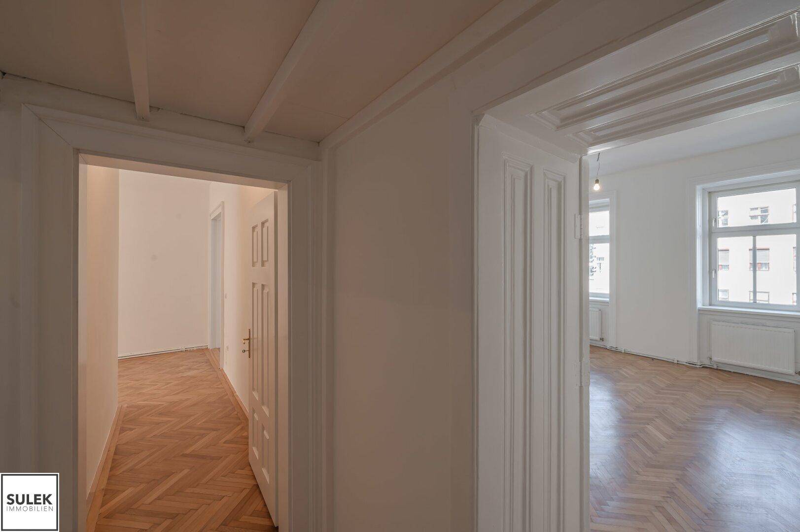 Flur mit Fischgrätparkett und Blick in angrenzende Zimmer mit hohen Decken.