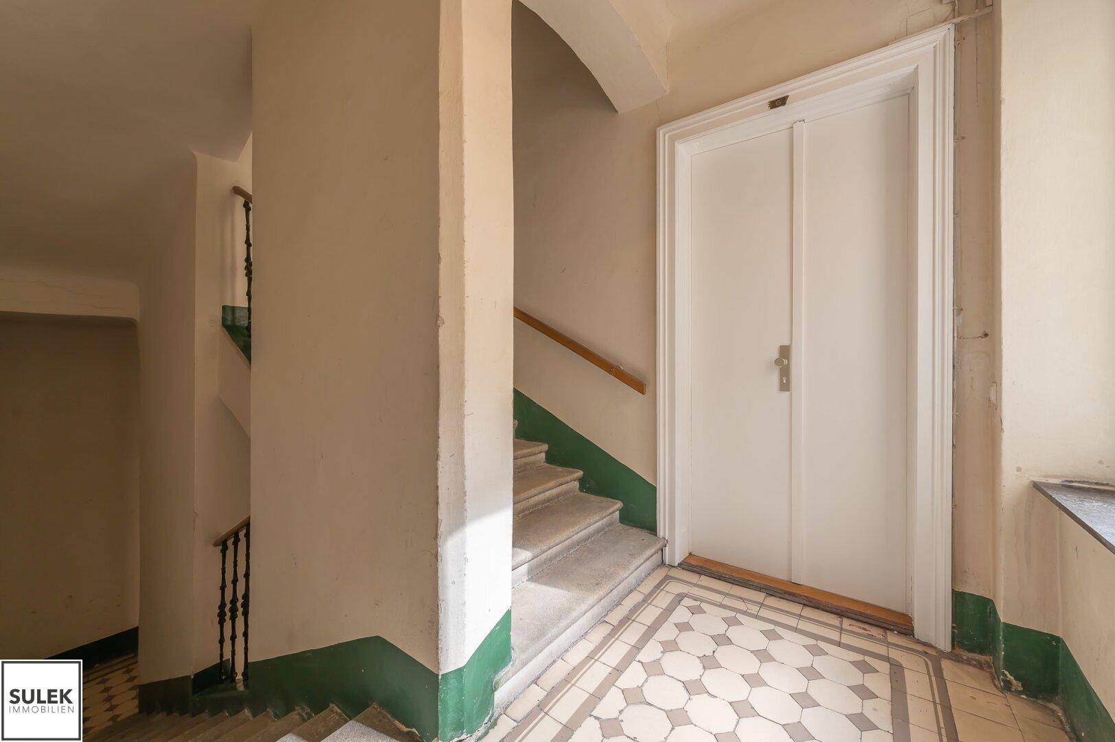 Historisches Treppenhaus mit gemusterten Fliesen und traditionellem Geländer im Eingangsbereich.