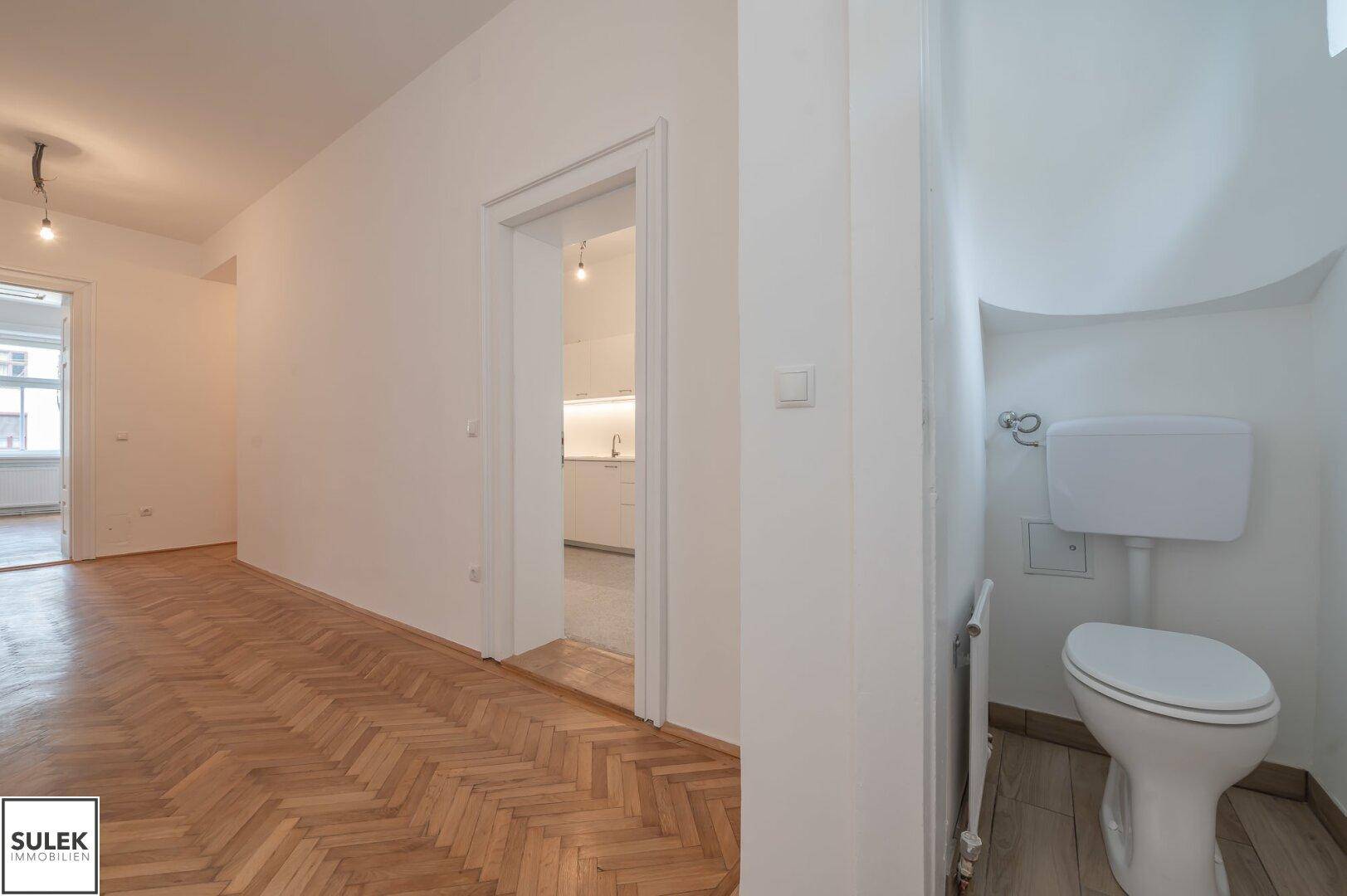 Kleines separates WC mit einfacher Toilette und weiß gefliesten Wänden.