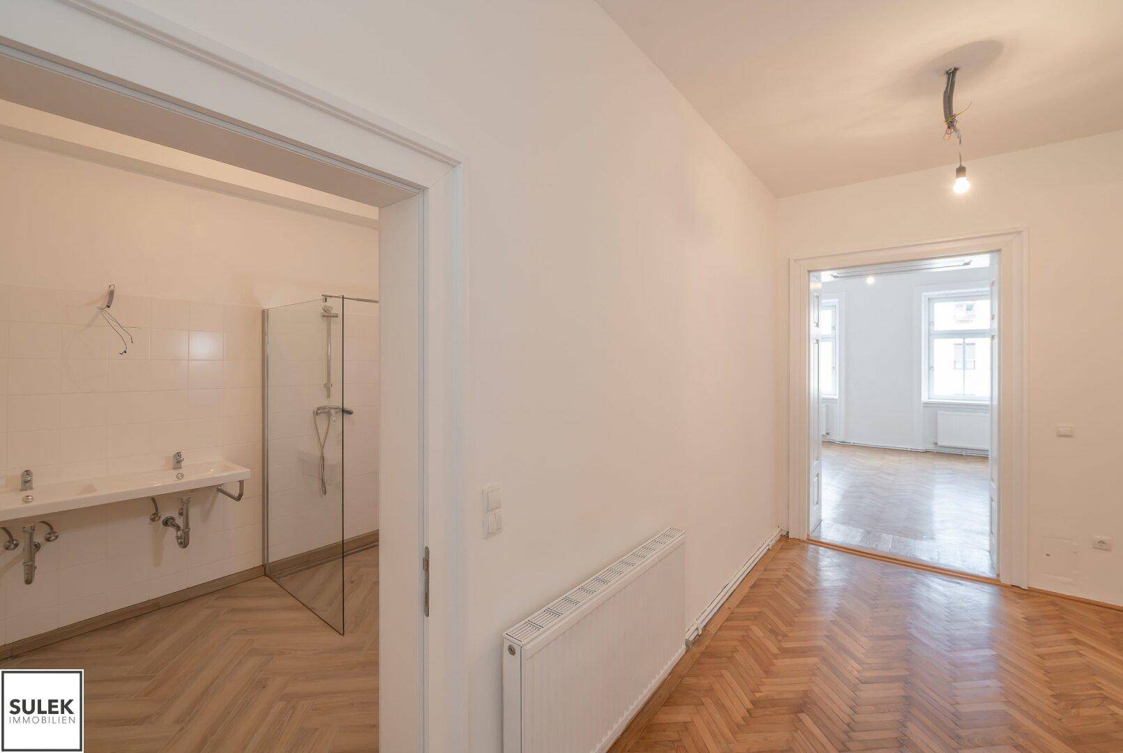 Badezimmer mit offener Duschkabine und zwei Waschbecken, angrenzend an einen Flur.