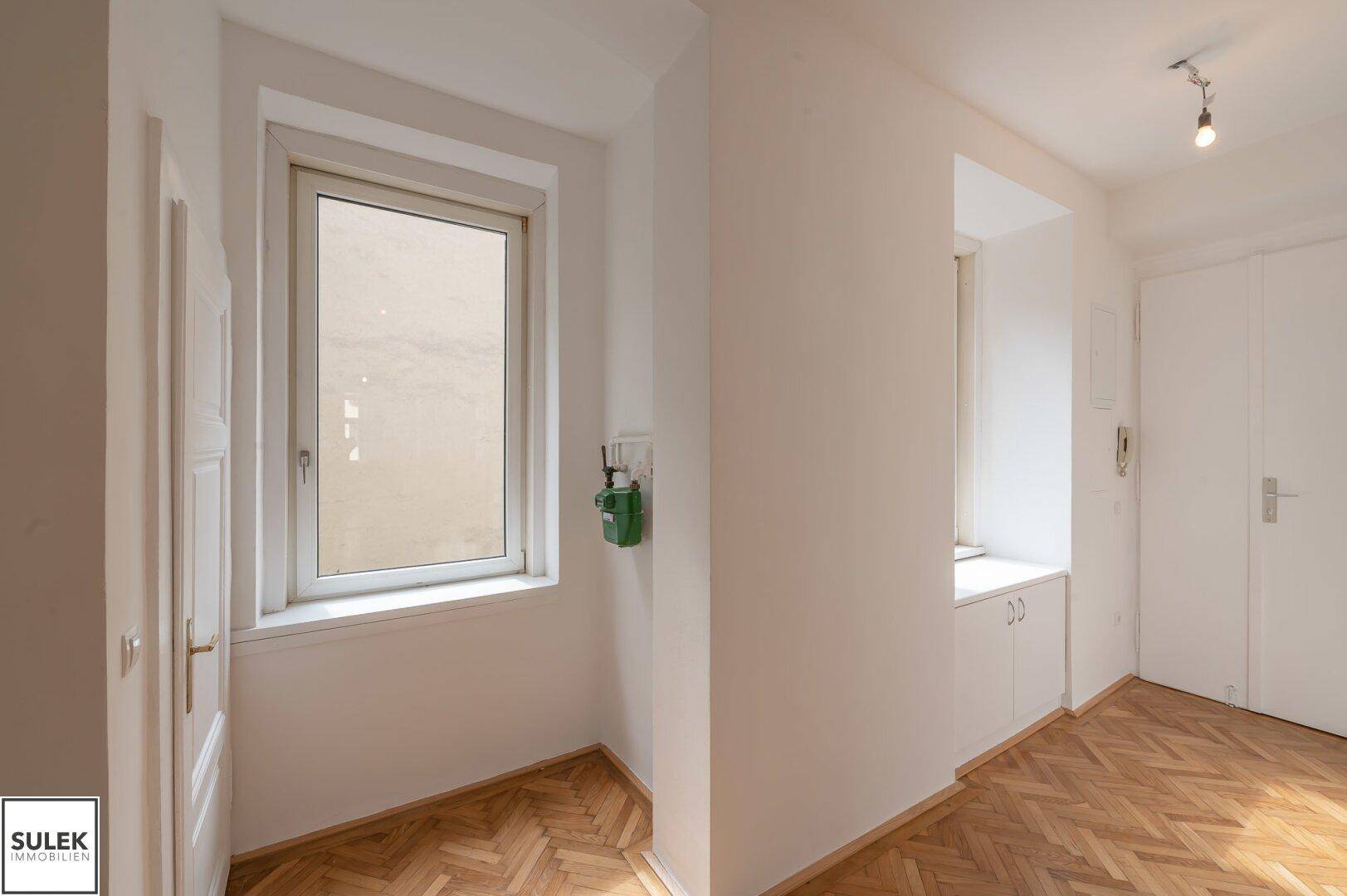 Heller Flur mit Fischgrätparkett, Fenster und integrierten Schränken für Stauraum.