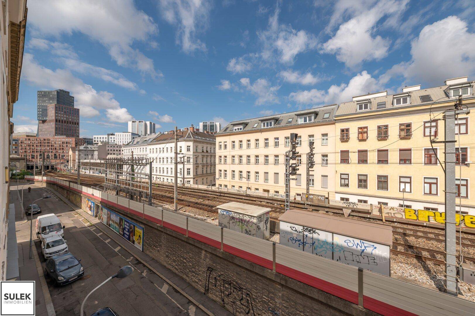 Blick auf die Stadt mit Bahngleisen und umliegenden Gebäuden unter blauem Himmel.