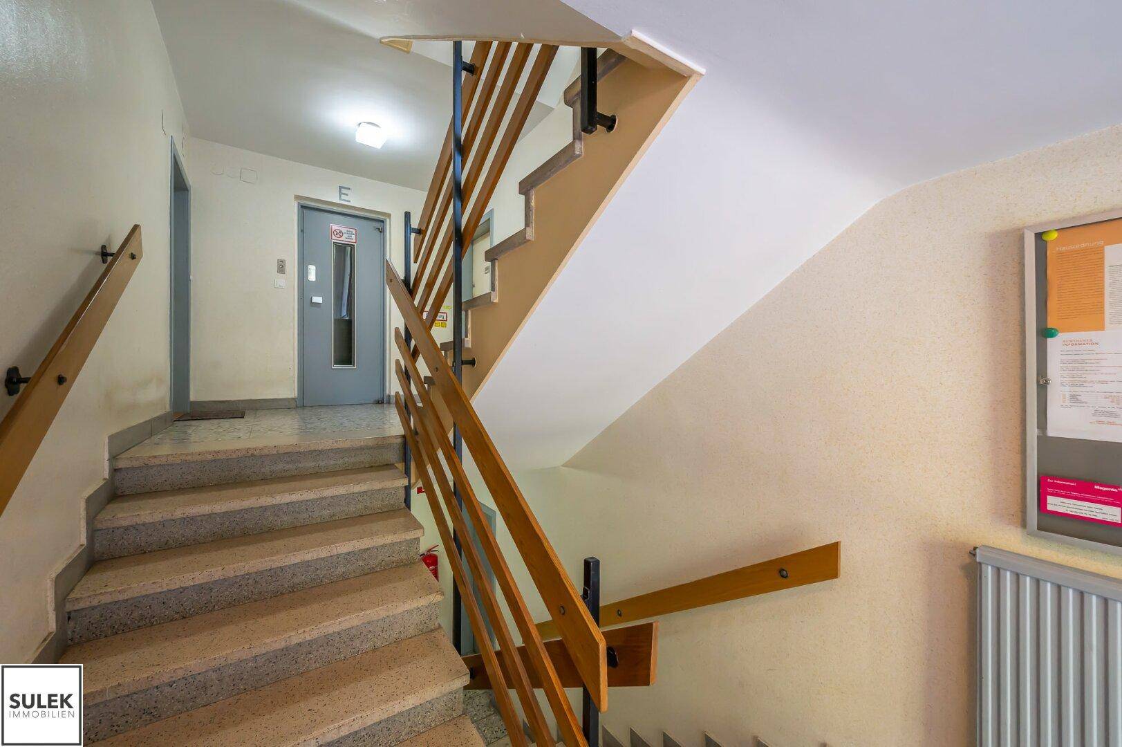 Treppenhaus mit Granitstufen und Holzgeländer, führt zu den oberen Etagen.