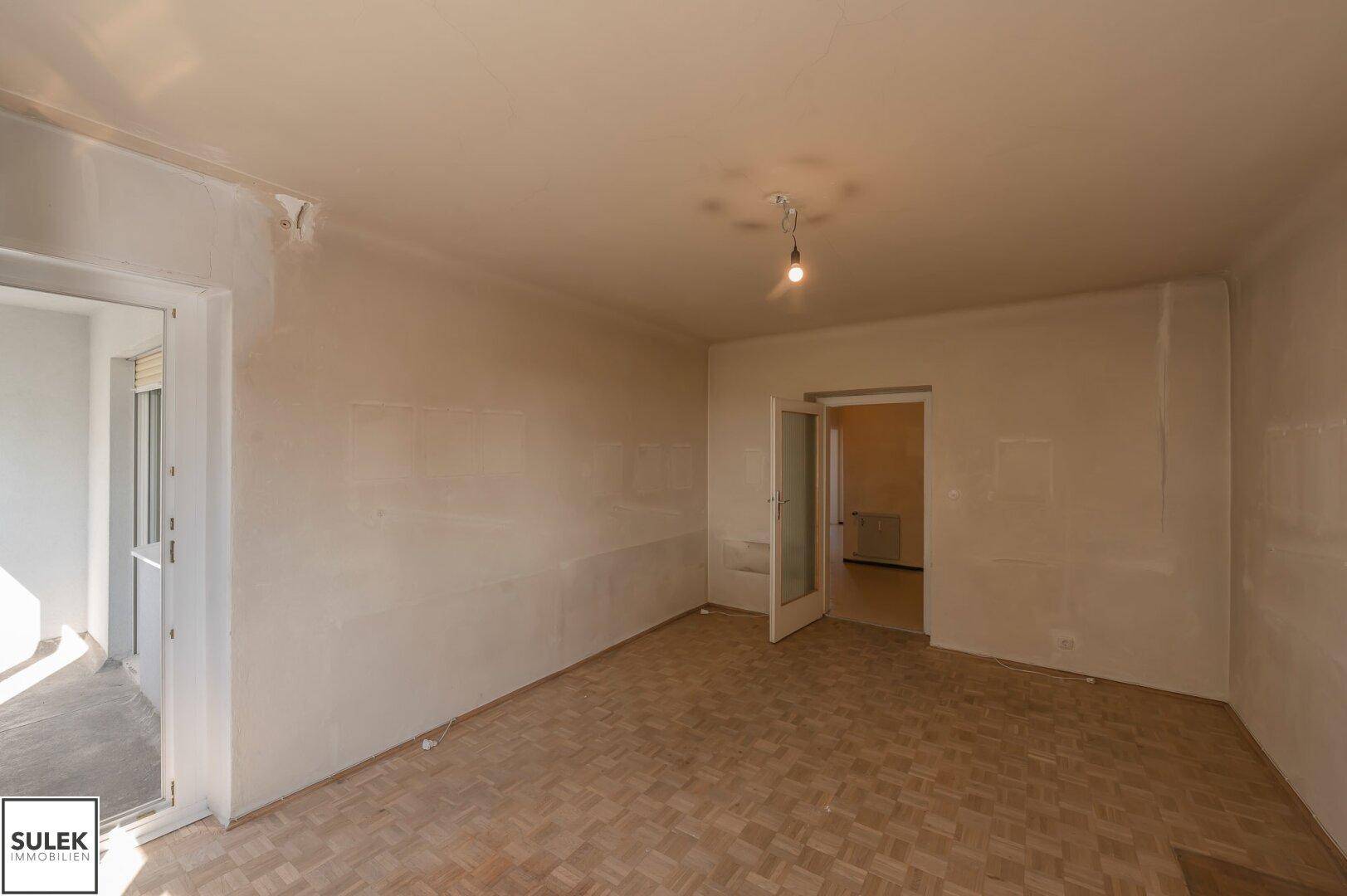Unmöbliertes Zimmer mit Parkettboden und Zugang zu einem sonnigen Balkon.
