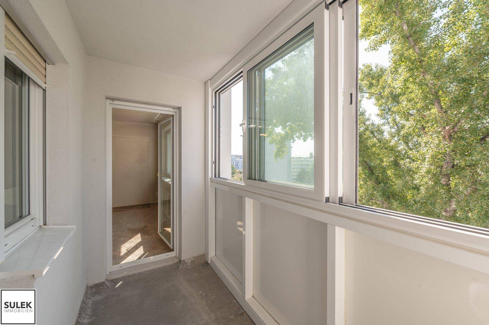 Verglaste Loggia mit Blick auf Bäume und die Stadt, ideal für entspannte Stunden.