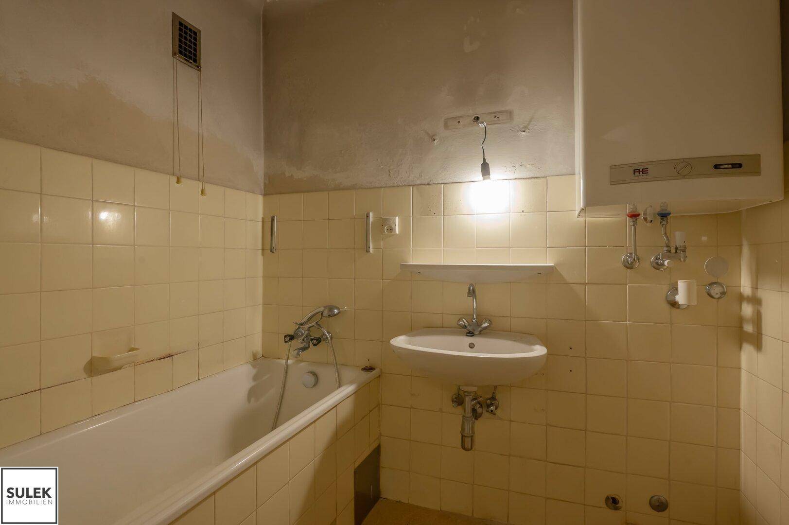Badezimmer mit Badewanne, Waschbecken und gelben Fliesen, renovierungsbedürftig.