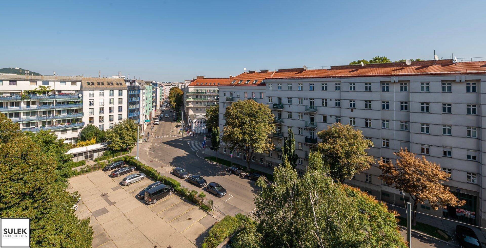 Weitläufiger Stadtblick mit Gebäuden, Straßen und Parkplätzen unter blauem Himmel.