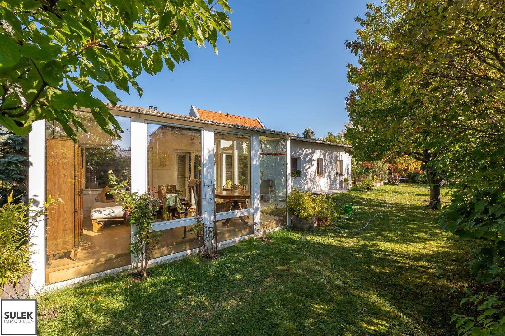 Sonniger Gartenbereich mit einem Wintergarten, der an das Wohnhaus angrenzt und viel Grün bietet.