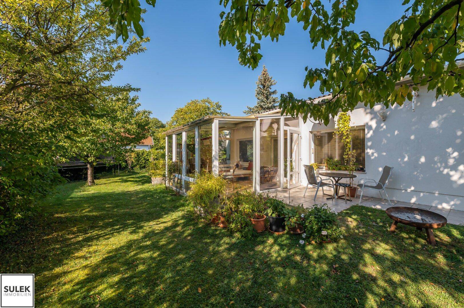 Großzügige Terrasse mit Sitzgelegenheiten und angrenzendem Wintergarten, umgeben von einem grünen Garten.