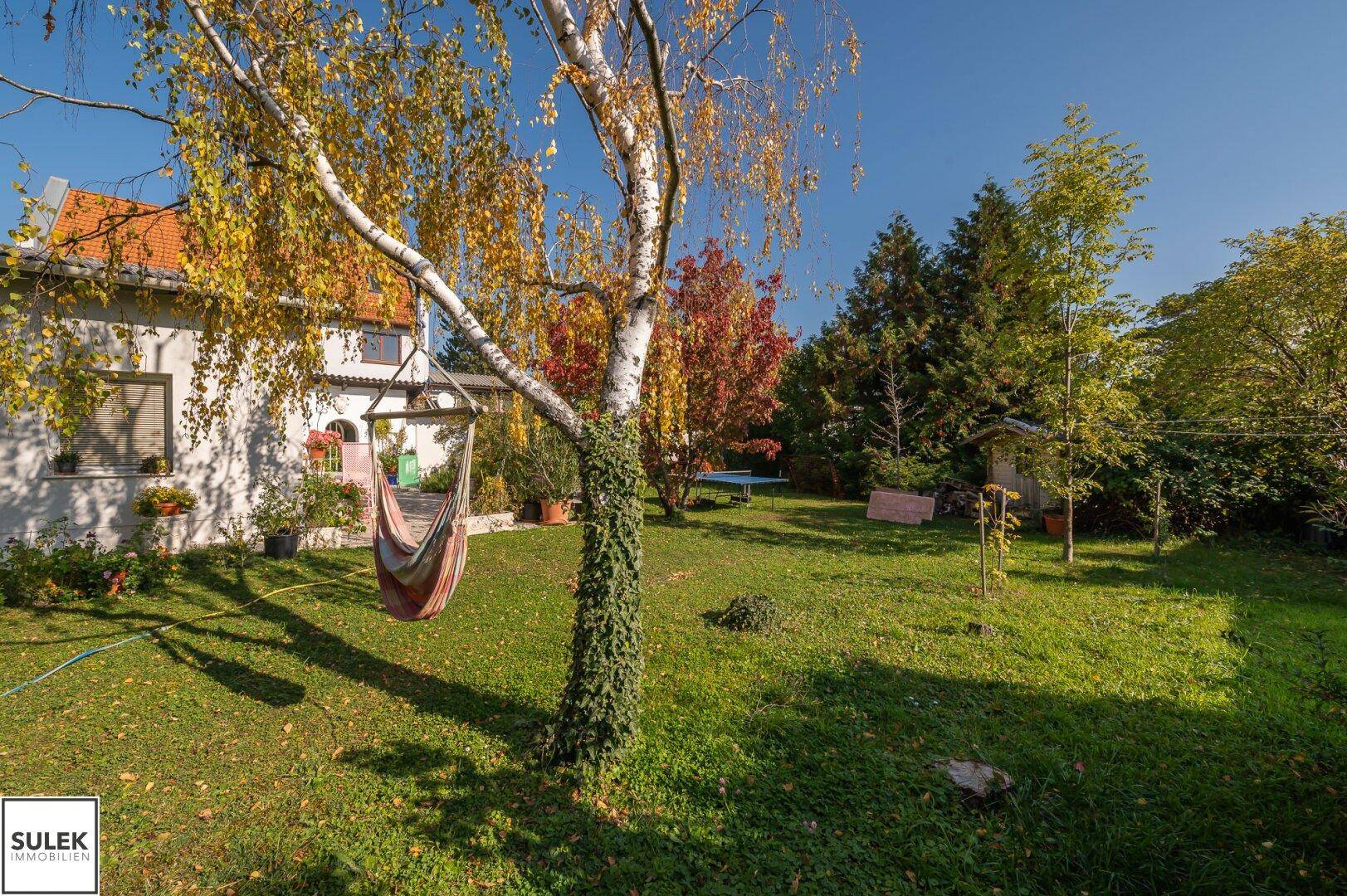 Großer, gepflegter Garten mit alten Bäumen, Rasenfläche und Hängematte, ideal zum Entspannen.