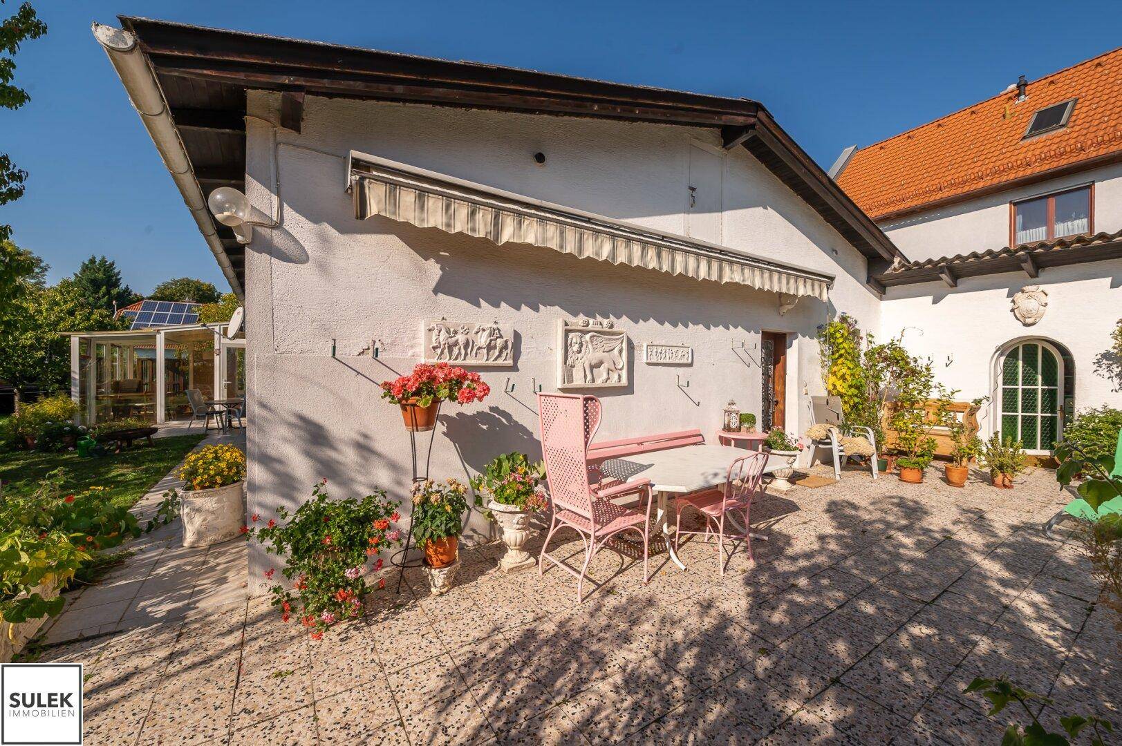 Sonniger Terrassenbereich mit Gartenmöbeln und Blumen, umgeben von üppigem Grün.