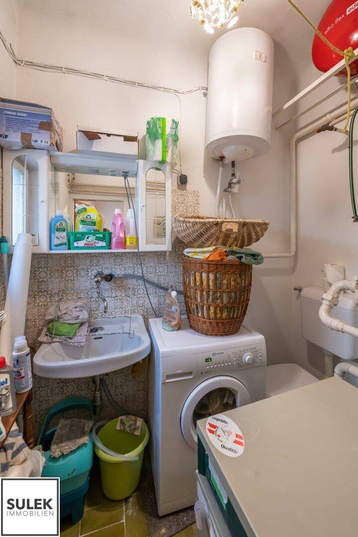 Funktionaler Hauswirtschaftsraum mit Waschmaschine, Spülbecken und Warmwasserboiler.