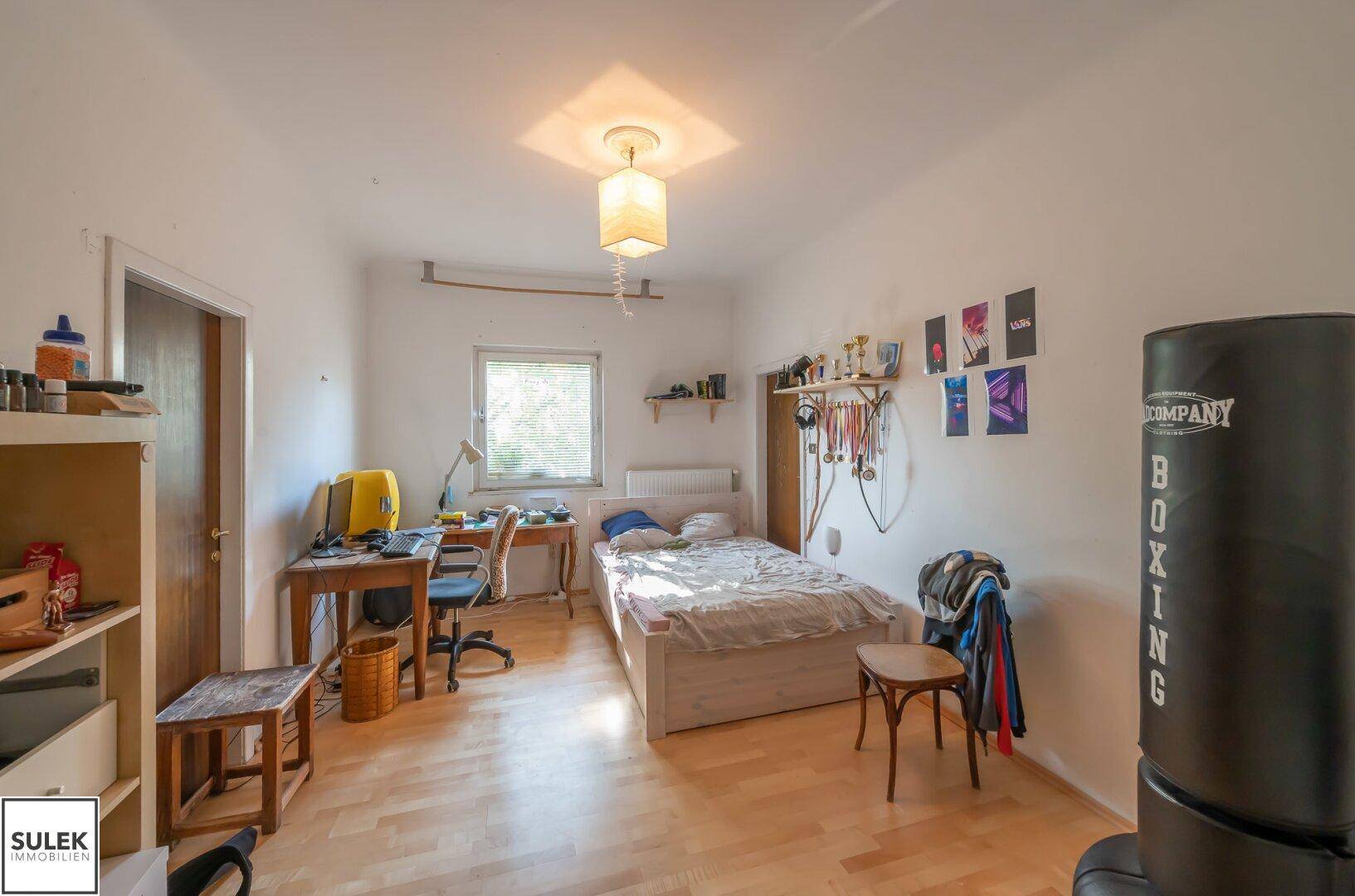 Helles Schlafzimmer mit Parkettboden, Schreibtisch und einem Boxsack für sportliche Aktivitäten.
