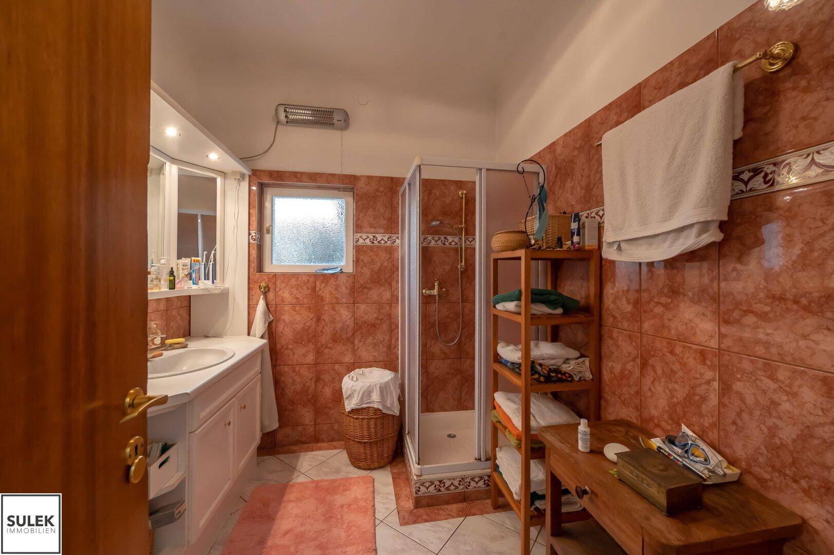 Badezimmer mit roten Fliesen, Duschkabine, Einzelwaschbecken und Fenster.