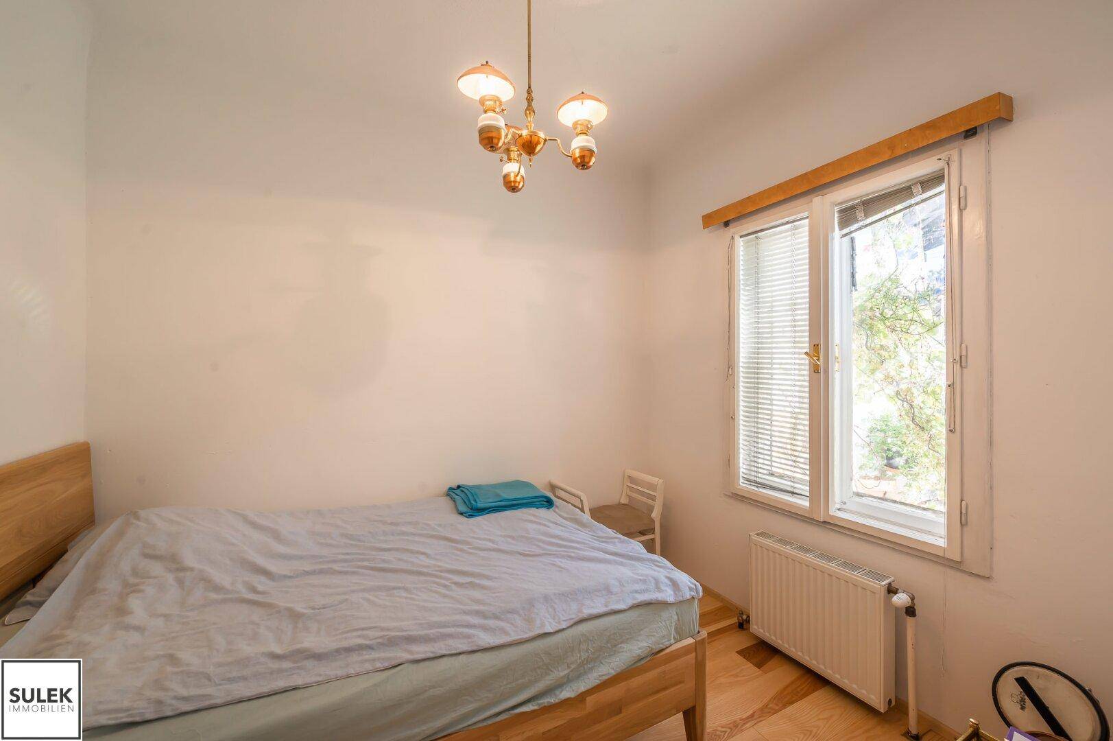 Gemütliches Schlafzimmer mit Parkettboden, großem Fenster und Heizkörper.