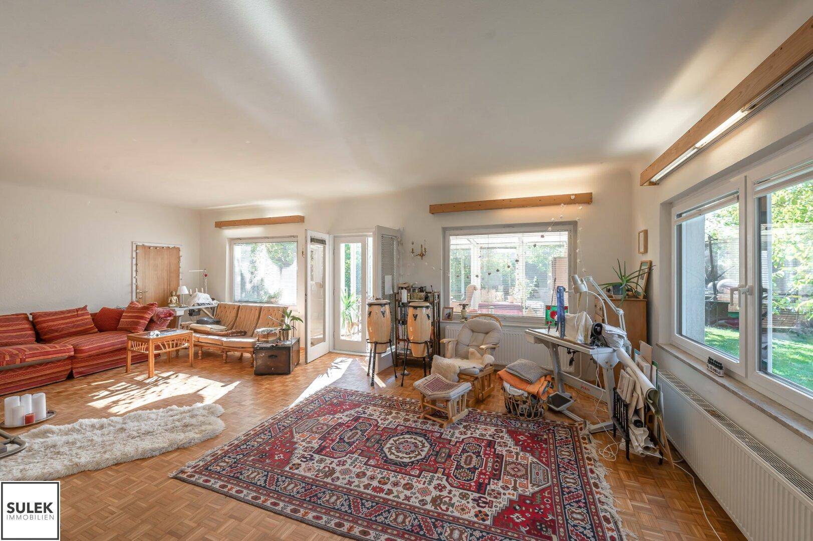 Helles Wohnzimmer mit Parkettboden, großen Fenstern und Zugang zum Wintergarten.