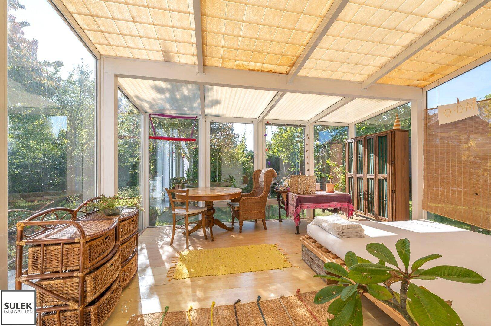 Geräumiger Wintergarten mit Glasfronten, Korbmöbeln und direktem Blick in den Garten.