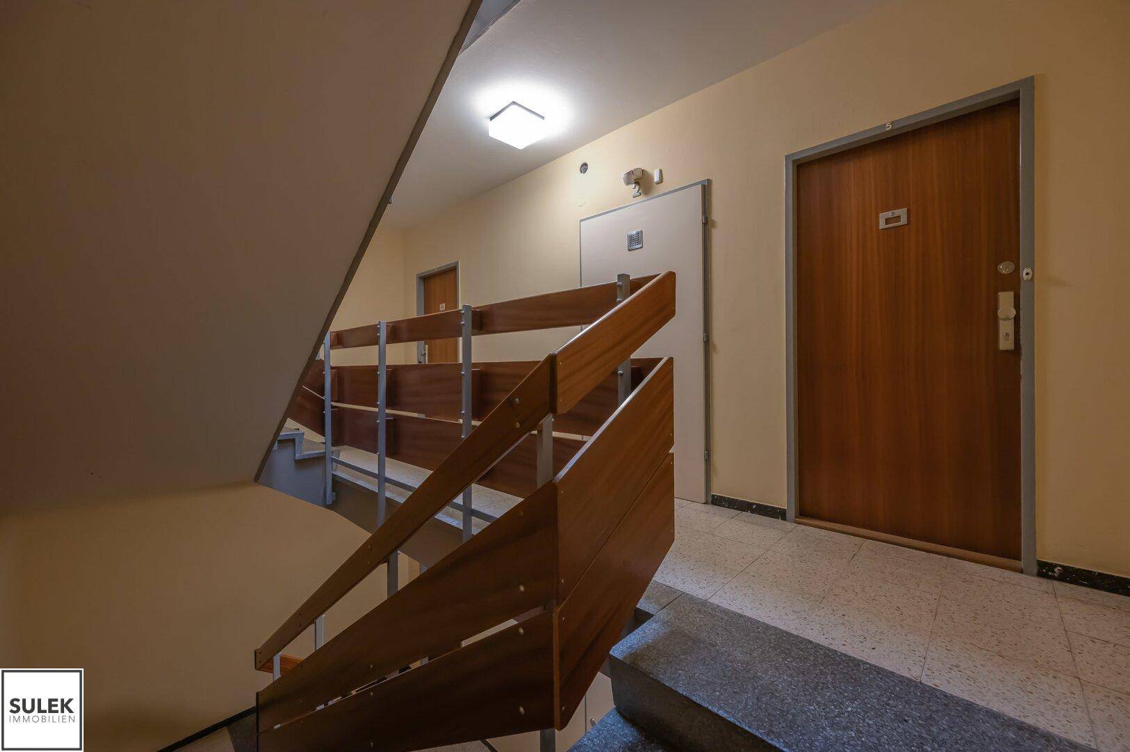 Treppenhaus mit Holzgeländer und Zugang zu den einzelnen Wohneinheiten.