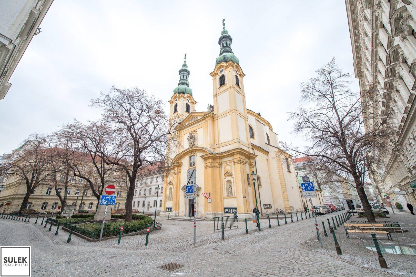 Historische Kirche mit zwei Türmen an einem belebten Stadtplatz.