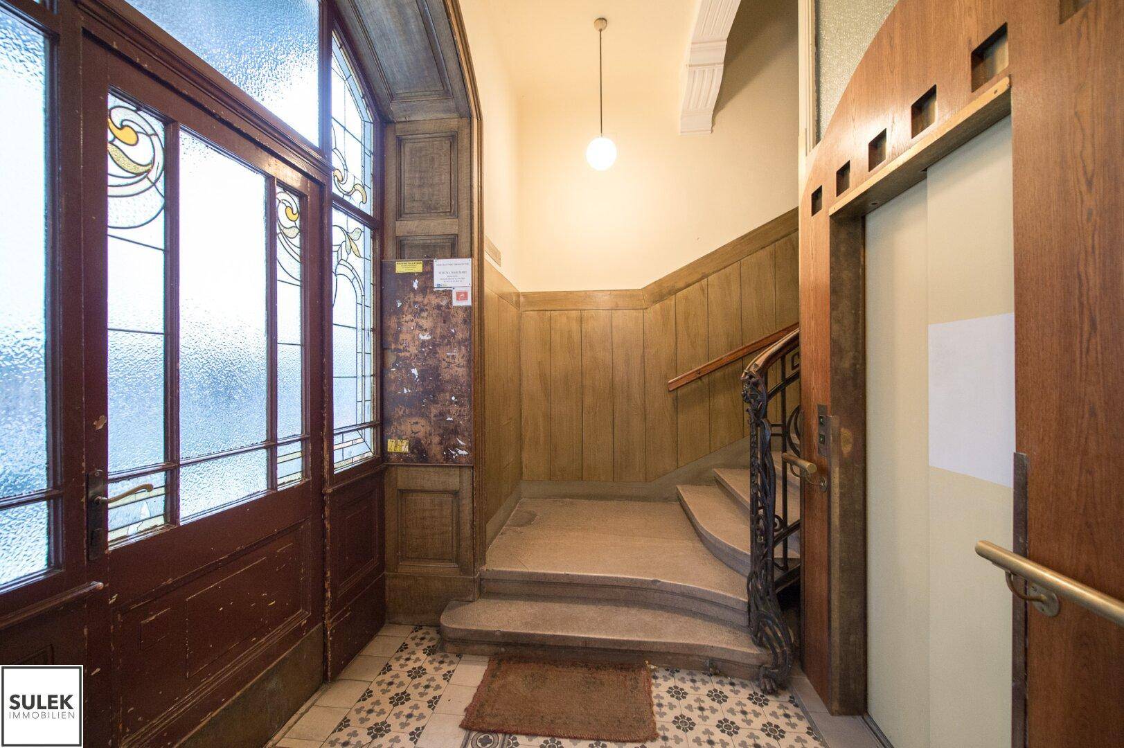 Historischer Eingangsbereich mit Holzvertäfelung, Buntglasfenstern und Aufzug.