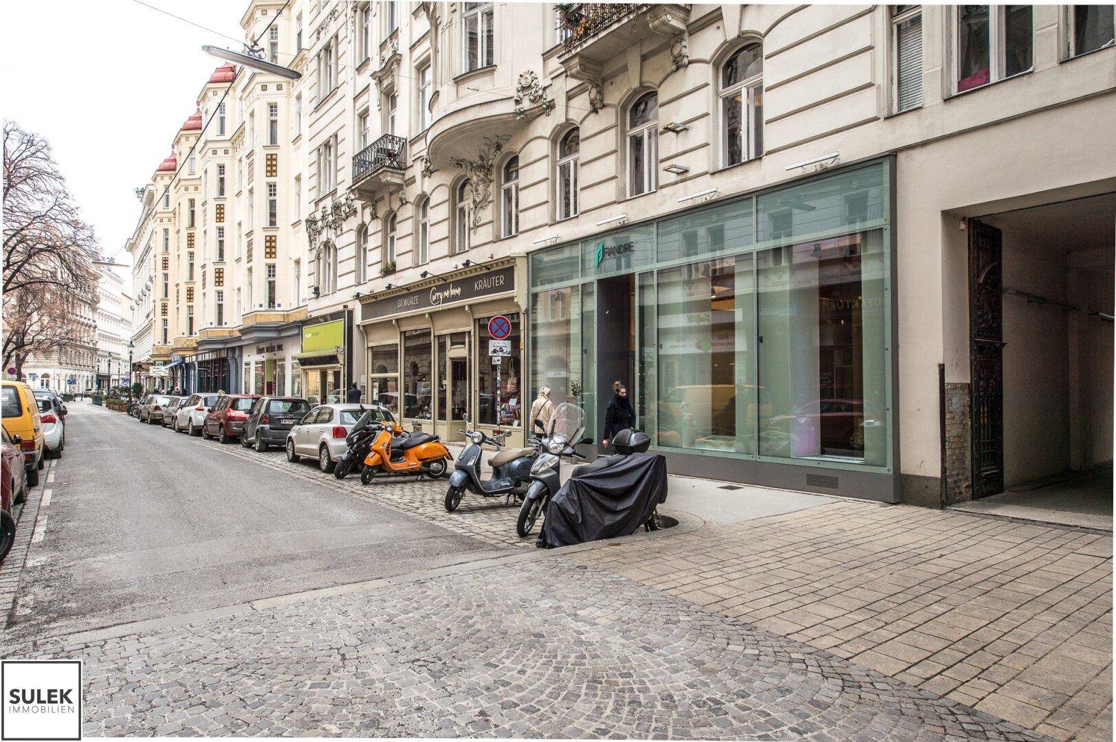 Belebtes Stadtviertel mit parkenden Autos und historischen Gebäuden entlang der Straße.