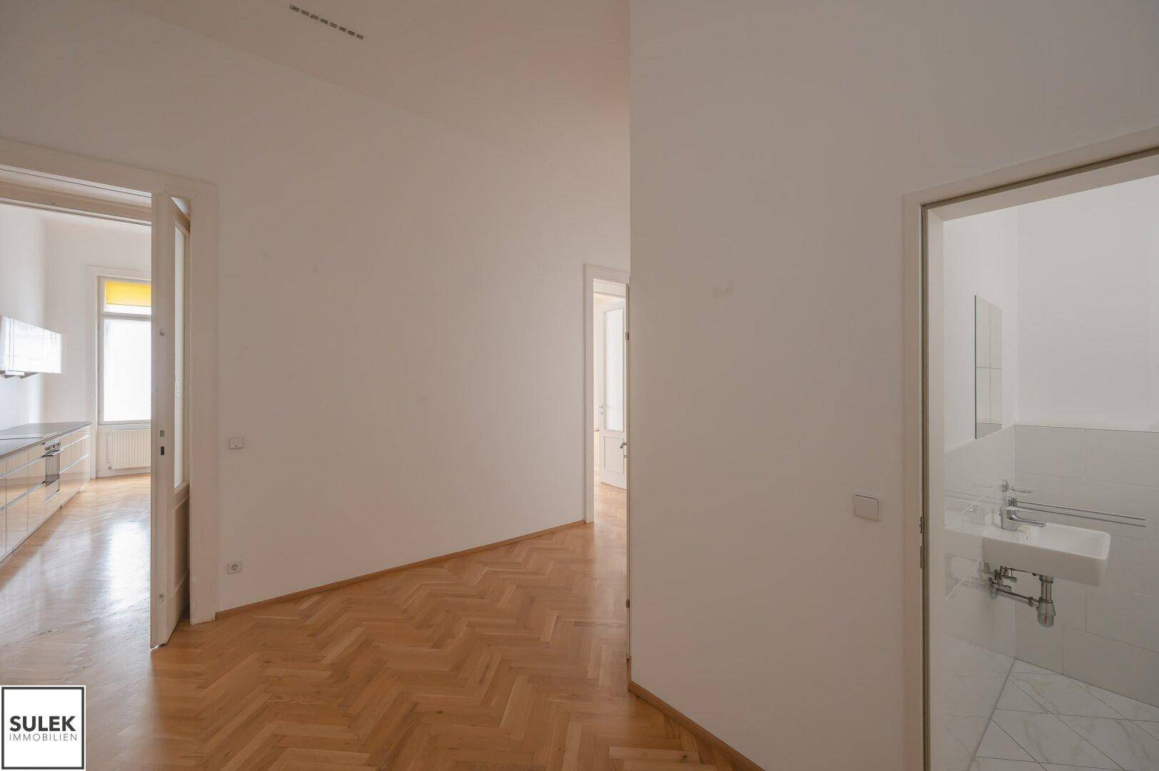 Gangbereich mit Fischgrätparkett, der zur Küche und zum Badezimmer führt.