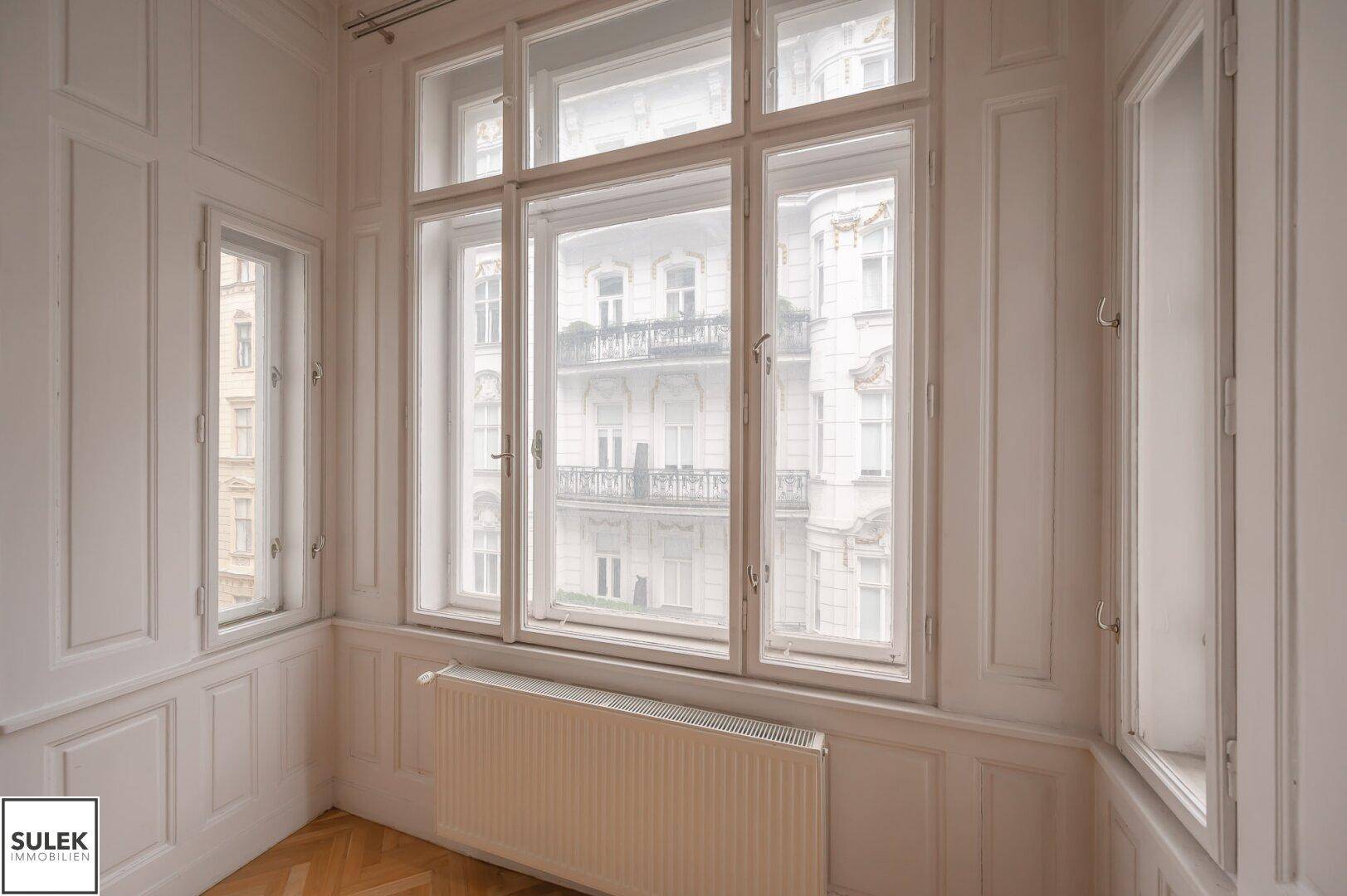 Detailansicht der hohen Fenster mit klassischer Holzvertäfelung und Blick auf die Stadt.