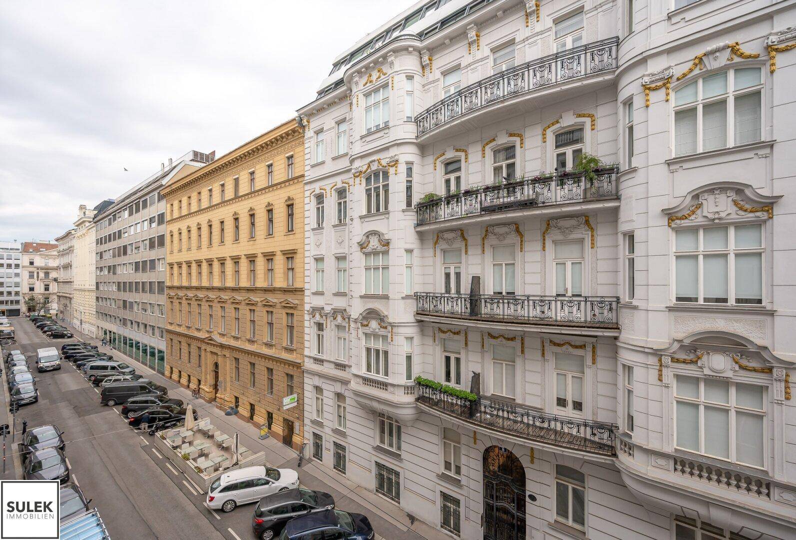 Historische Gebäudezeile mit klassischen Fassaden und Balkonen entlang einer belebten Straße.