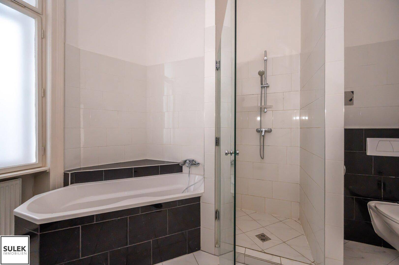 Badezimmer mit Eckbadewanne, Duschbereich und kontrastierenden Fliesen.