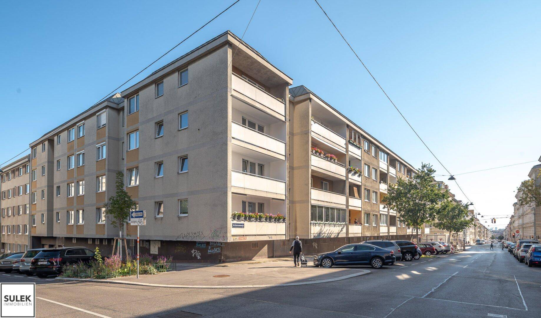 Außenansicht eines Mehrfamilienhauses mit Balkonen und parkenden Autos an der Straße.