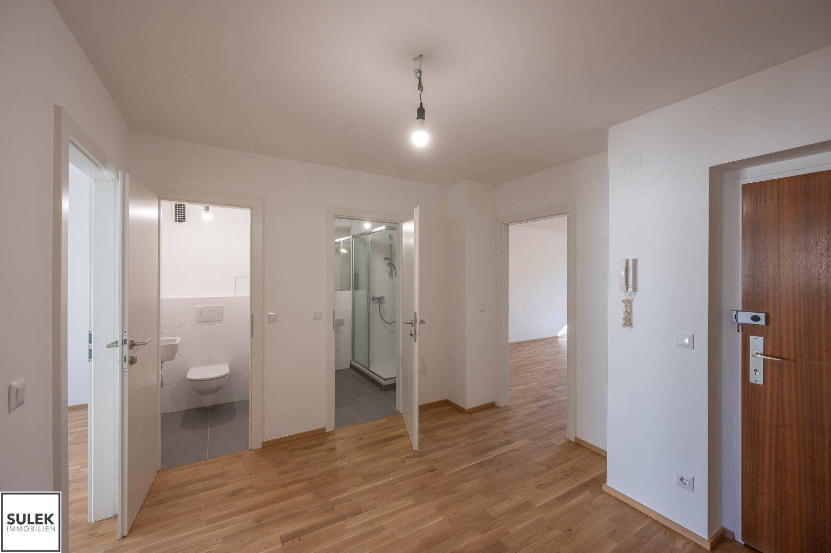 Eingangsbereich mit Holztür und Zugang zu einem Badezimmer und einem separaten WC.
