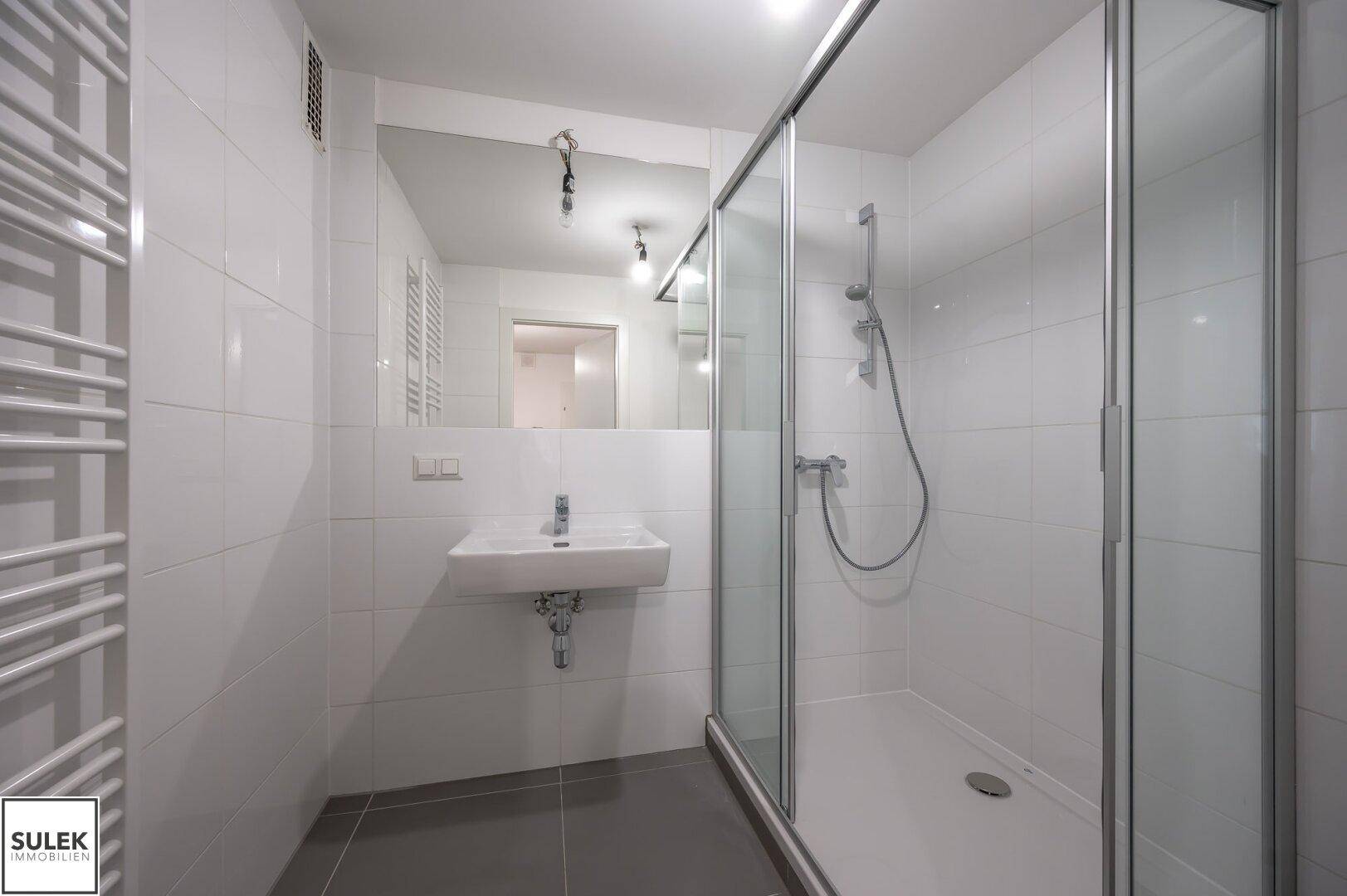 Modernes Badezimmer mit weißen Fliesen, Duschkabine, Waschbecken und beheiztem Handtuchhalter.