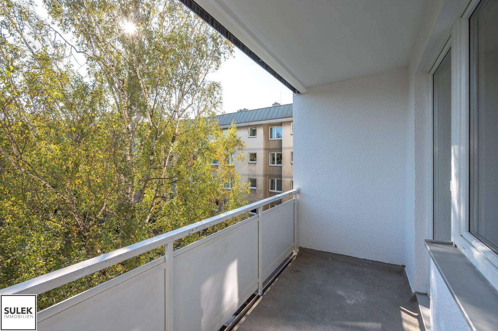 Sonniger Balkon mit Blick auf Bäume und ein gegenüberliegendes Gebäude, bietet Privatsphäre.