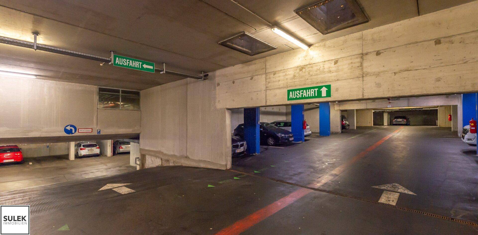 Geräumige Tiefgarage mit mehreren geparkten Fahrzeugen und Ausfahrtsschildern.