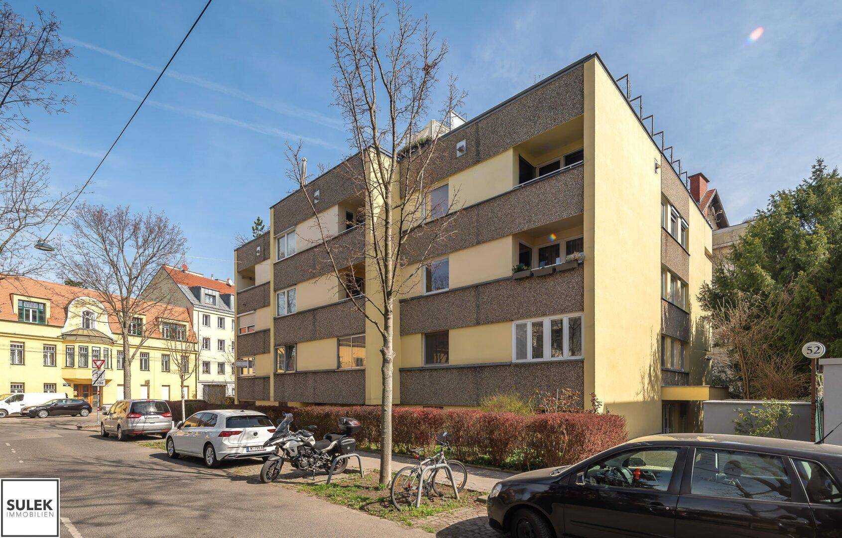 Mehrfamilienhaus mit gelber Fassade und Balkonen an einer ruhigen Straße.