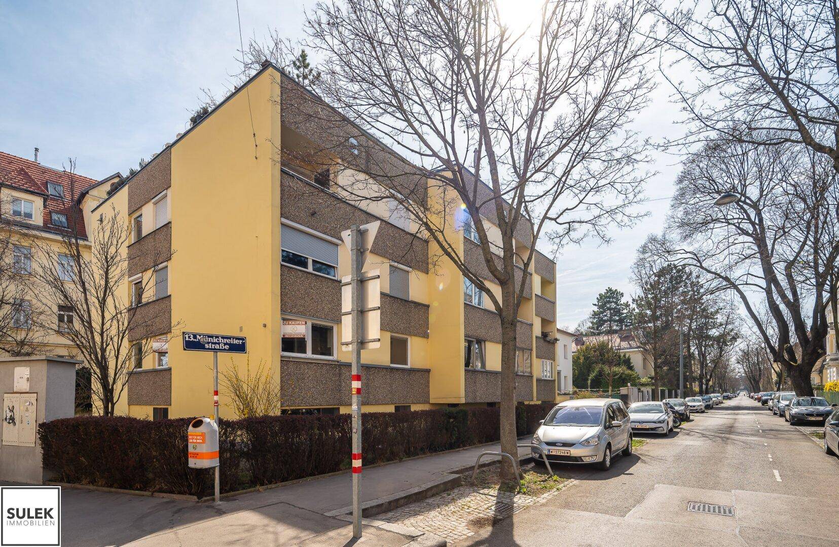 Wohngebäude mit gelber Fassade und Bäumen entlang der Straße.