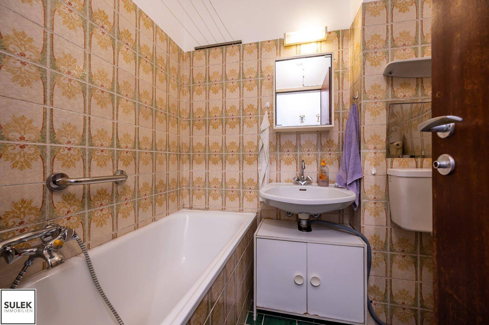 Badezimmer mit Badewanne, Waschbecken und gemusterten Wandfliesen im Vintage-Stil.