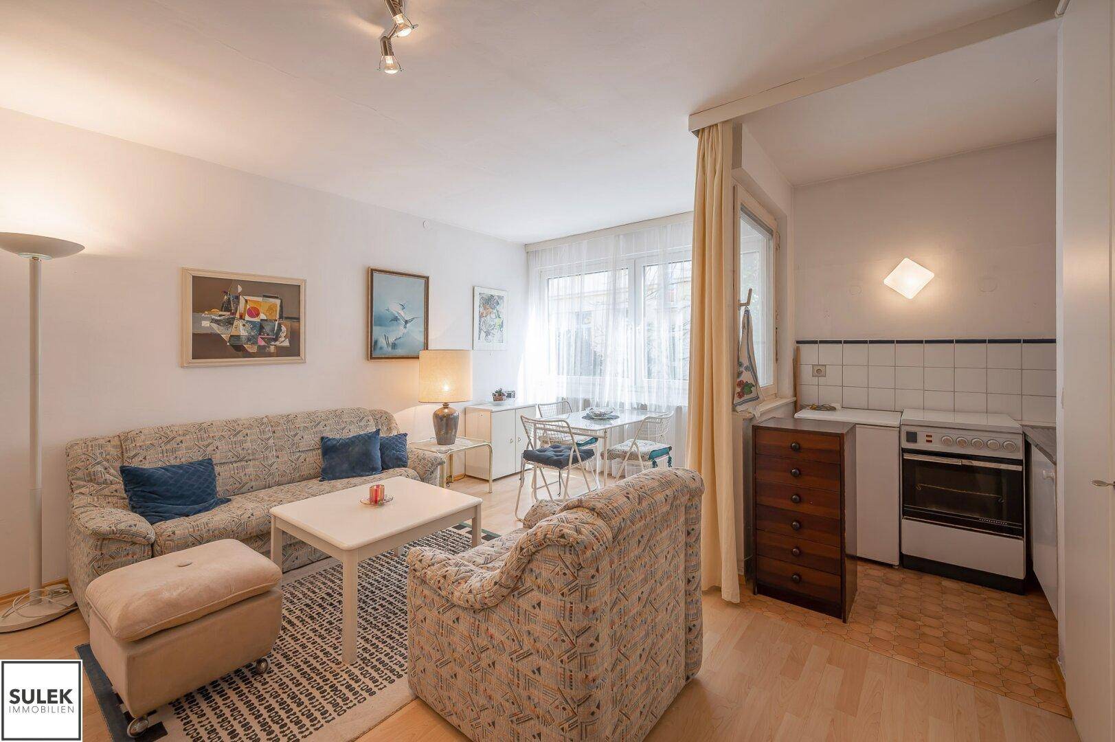 Offener Wohnbereich mit Sofa, Esstisch und kleiner Küchenzeile.