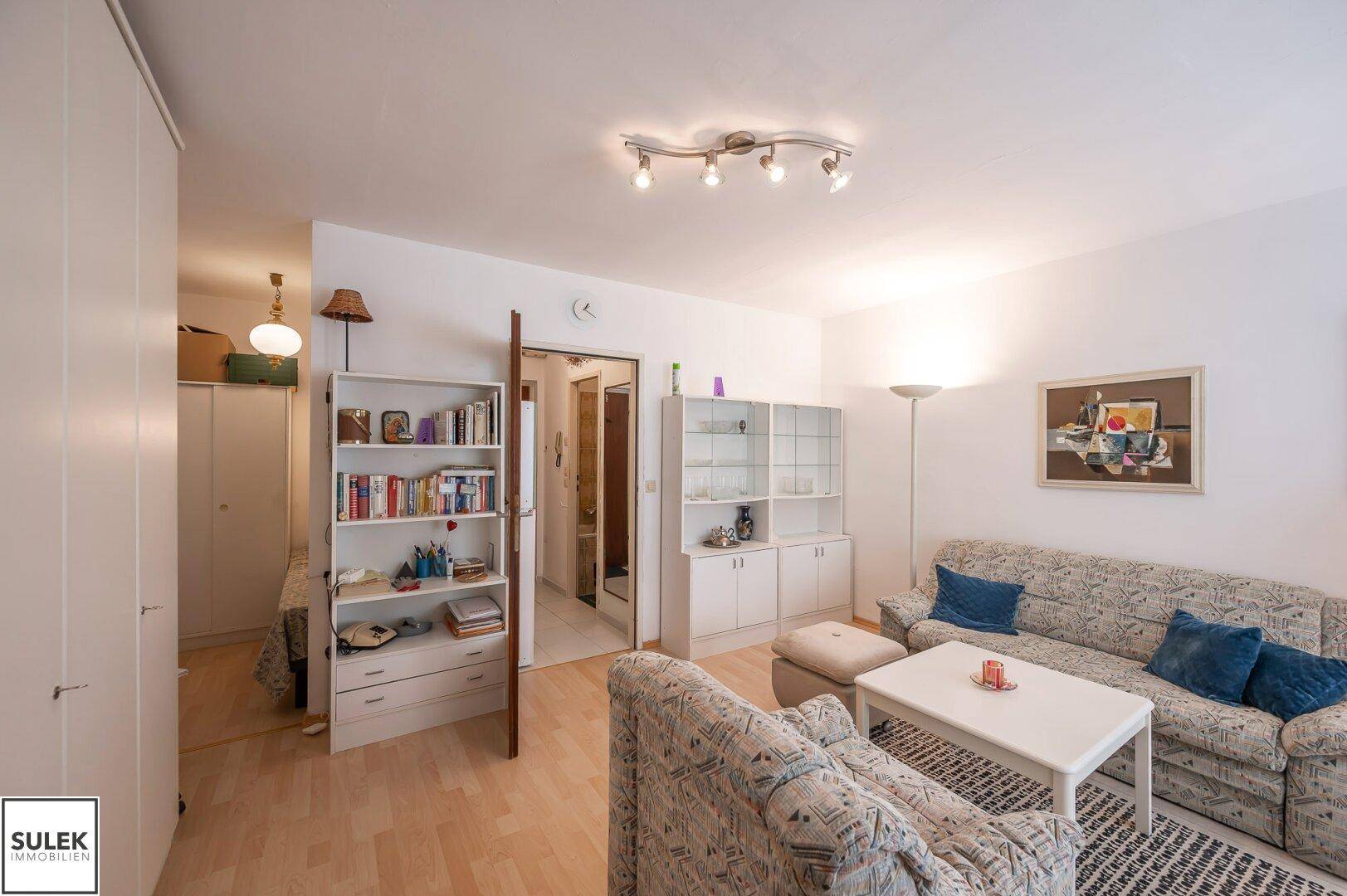 Wohnzimmer mit Parkettboden, Regalen und Zugang zu weiteren Räumen.