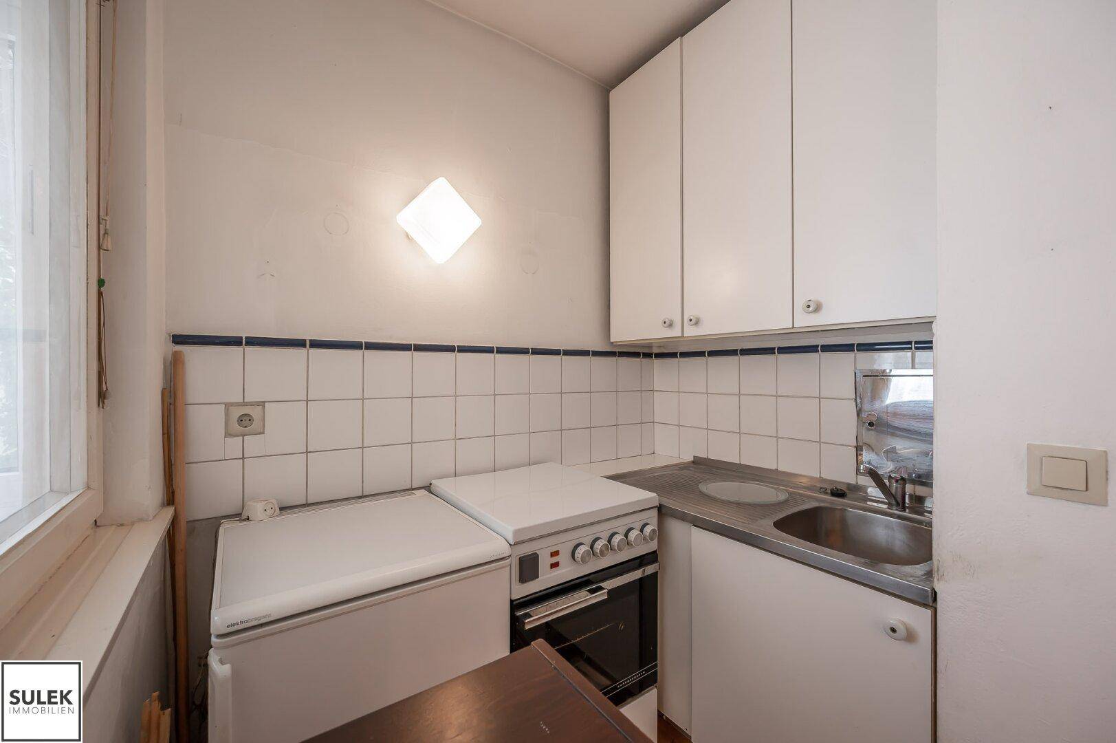 Kleine Küchenzeile mit Spüle, Herd und Kühlschrank in weißer Ausführung.